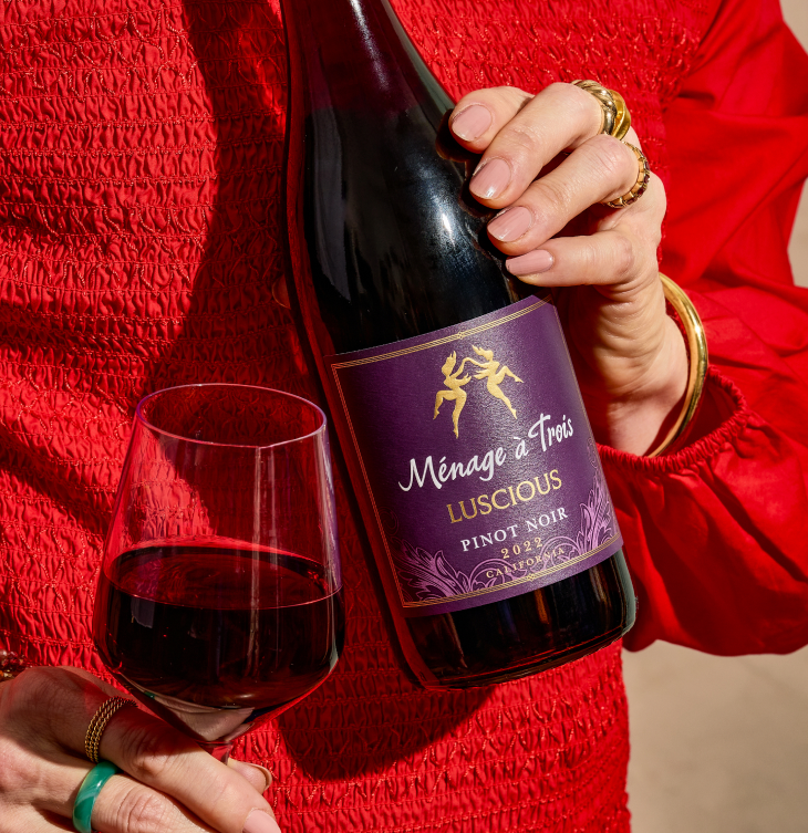Person holding a bottle of Ménage à Trois Luscious Pinot Noir and a glass of red wine