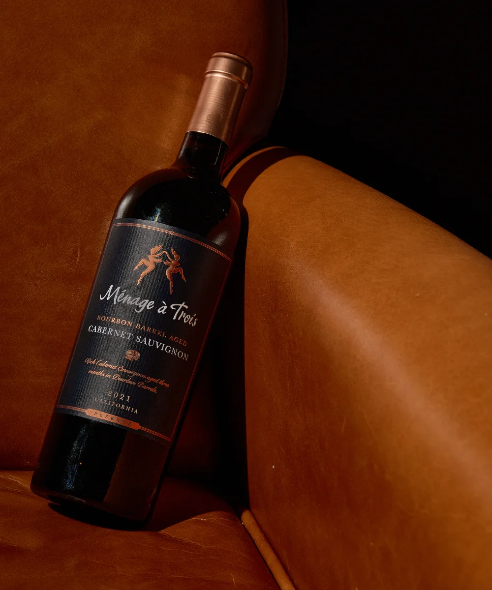 Bottle of Ménage à Trois Bourbon Barrel Aged red wine resting on an orange armchair